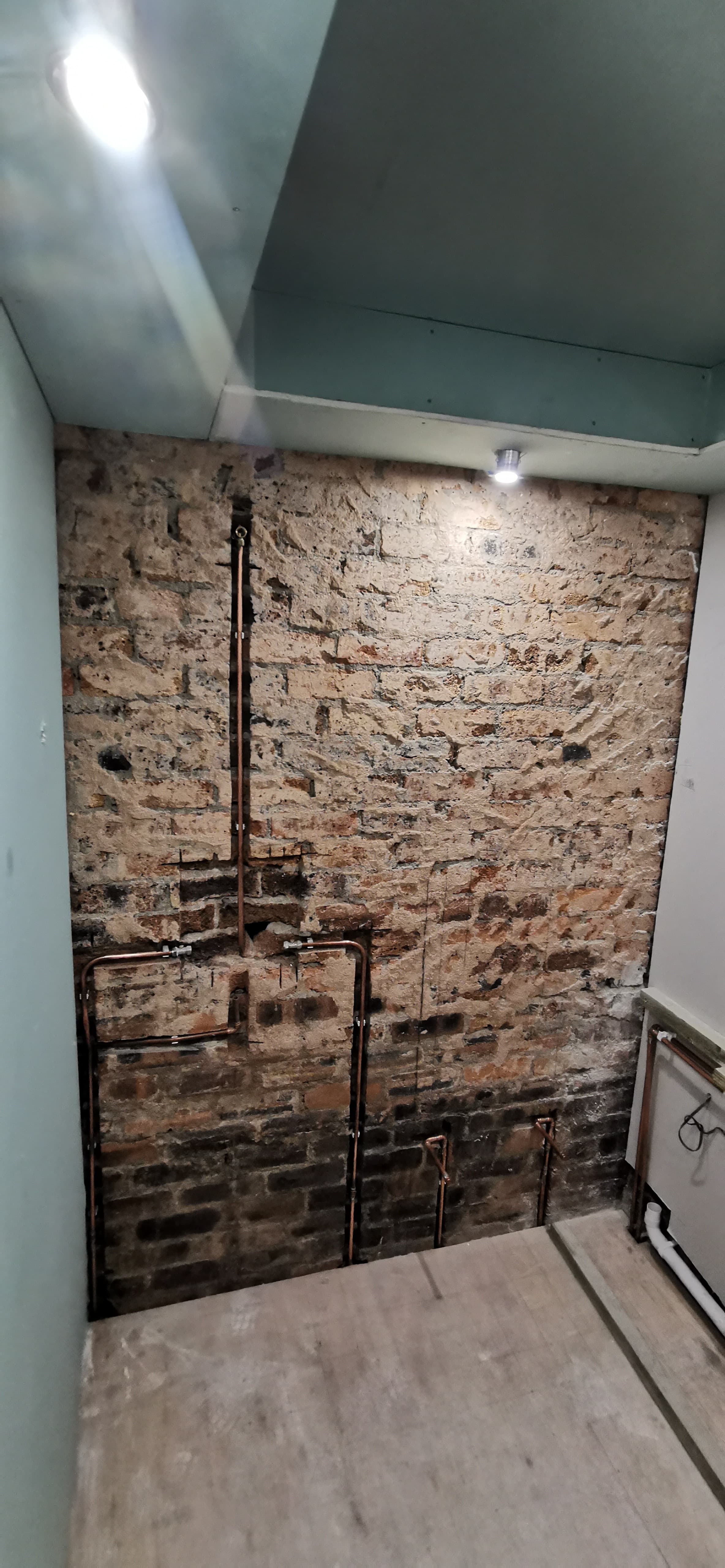 Bathroom refit first-fix stage with pipework run to exposed brick wall